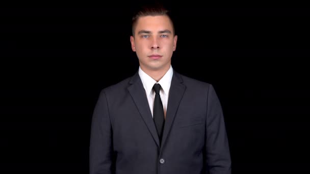 Jonge zakenman shows als bij de hand. Man in een zwart pak op een zwarte achtergrond — Stockvideo