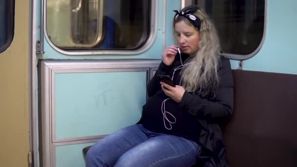 Беременная женщина разговаривает по телефону через наушники с поездом метро. Старый вагон метро — стоковое видео