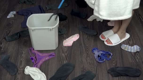 Aufräumen der verstreuten schmutzigen Dinge im Raum. Reinigung mit speziellen Handmilben. Socken und Unterhosen liegen auf dem Boden. Eine Frau im weißen Mantel packt Dinge in einen Eimer — Stockvideo
