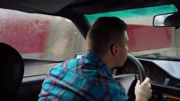 Молодой человек водит машину. Дождливая погода. Вид на человека сзади с заднего сиденья — стоковое видео