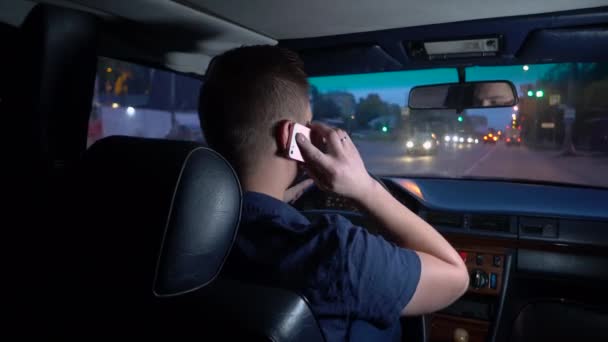 Молодой человек водит машину и говорит по телефону. Вид на человека сзади с заднего сиденья — стоковое видео