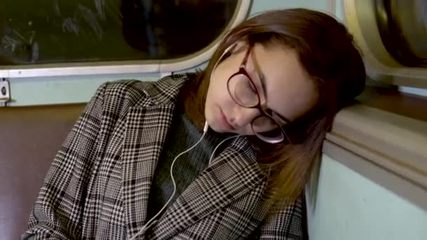 若い女性が地下鉄の電車の中で眠ってしまった。耳にヘッドホン付きの女の子。旧地下鉄車 — ストック動画