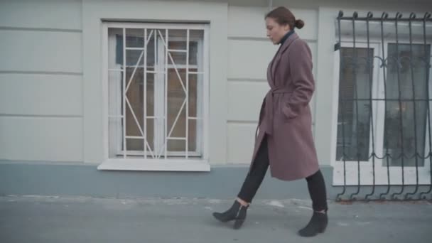 Dziewczyna w liliowym płaszczu chodzi ulicami starego miasta. — Wideo stockowe