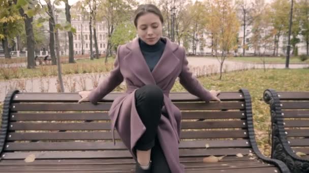 Het meisje in de jas zette een voet op de bank in het park — Stockvideo