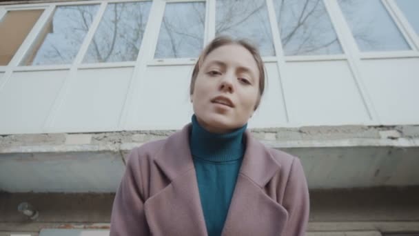 La chica con el abrigo púrpura está de pie sobre el fondo del antiguo edificio y se ve. El marco se aleja de la chica — Vídeos de Stock