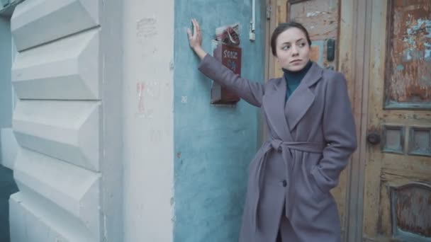 Το κορίτσι με το λιλά παλτό στέκεται στο δρόμο στην πόρτα του παλιού κτιρίου. — Αρχείο Βίντεο