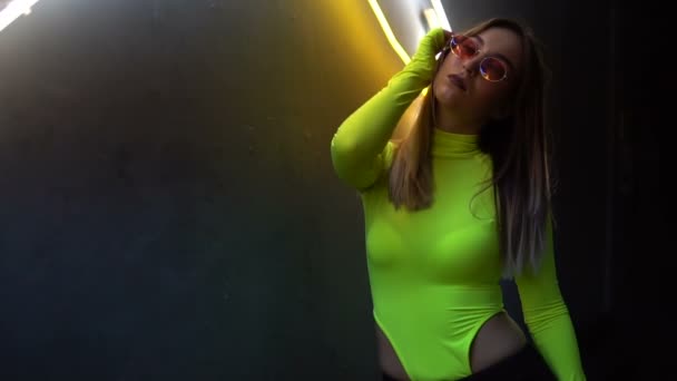 Fashionable girl in a body on a background of a neon lamps. The glasses reflect the lamp — Stock Video