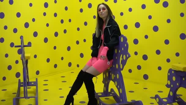 La ragazza alla moda siede su un cavallo di legno su uno sfondo giallo — Video Stock