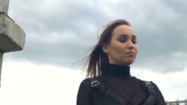 Chica sobre un fondo de nubes grises. Cabello revoloteando en el viento. Movimiento lento — Vídeos de Stock