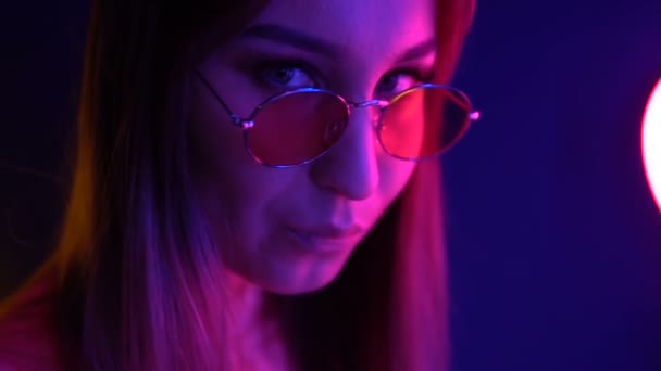 Fata la modă în ochelari pe un fundal de neon. Inimile de neon sunt reflectate în ochelari . — Videoclip de stoc