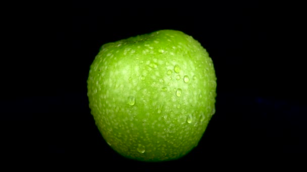 Water is sprayed on a green apple. On a black isolated background — Stock Video