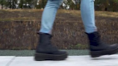 Bir kadın büyük siyah botlarla beton bir çit boyunca yürür. Yakın plan.
