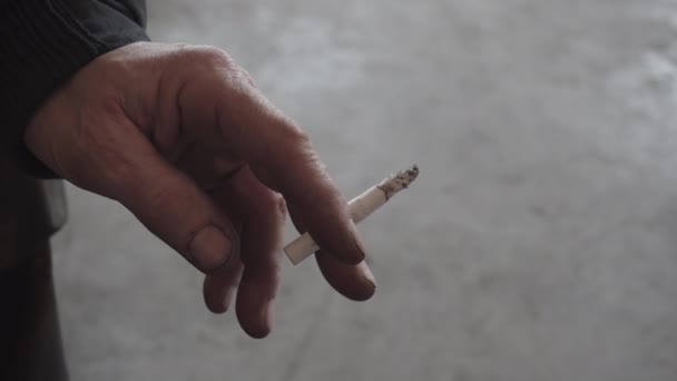 An elderly man holds a smoldering cigarette in his hand. Hand of an old man close-up — Stock Video