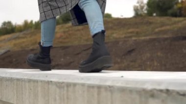 Bir kadın büyük siyah botlarla beton bir çit boyunca yürür. Yakın plan.