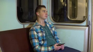 Genç bir adam metroda kulaklıkla müzik dinler. Eski metro vagonu