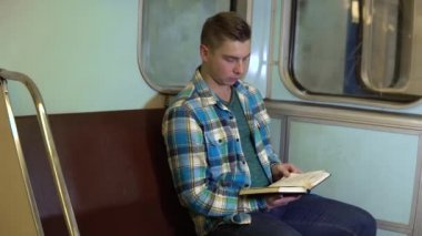 Genç bir adam metroda kitap okuyor. Eski metro vagonu