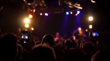 Bir müzik konserindeki bir kalabalık ellerini kaldırdı. Parlak renkli sahne ışıkları önünde gülen bir kalabalık. Konser kalabalığının siluetleri sahne ışıklarının önünde. Yavaş çekim