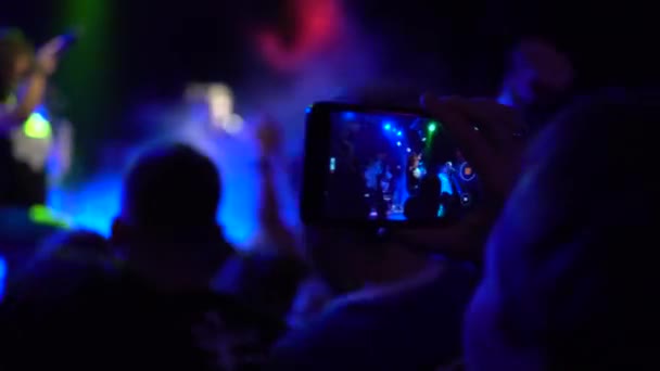 Samara, Oroszország - 2019. szeptember 29.Egy férfi egy zenei koncerten videót készít egy okostelefonon. A nevető tömeg előtt fényes színes színpadi fények — Stock videók