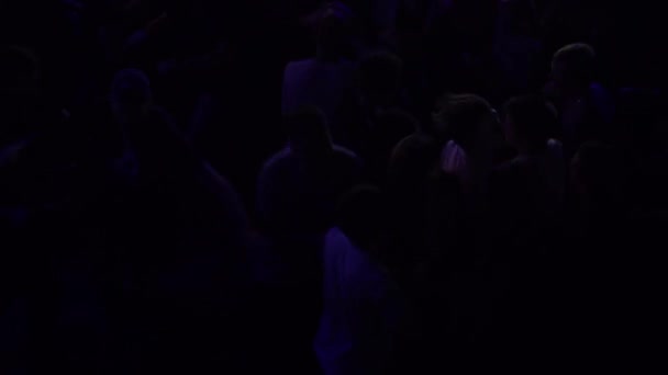 En folkmassa smäller till på en musikkonsert. En skrattande publik framför ljusa färgglada scenljus. Silhuetter av konserten publiken i främre scenen ljus — Stockvideo