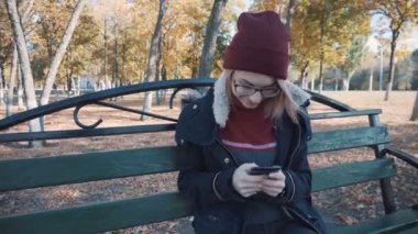 Parktaki bankta telefonunla oturan kız. Ceketli ve şapkalı kız.