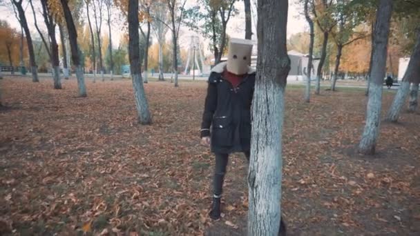Dziewczyna z paczką na głowie chowa się za drzewem. Dziewczyna w kurtce — Wideo stockowe