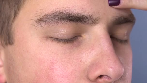 A young man plucked eyebrows in a spa salon. Woman tweezers pulls out eyebrows. Face close up — Stock Video