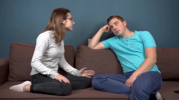 A young woman shouts at a young man. A man does not pay attention to a woman. Sitting on the couch — ストック動画