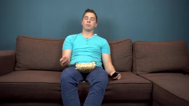 Mladý muž se dívá na televizi a jí popcorn. Ten chlap chytá popcorn pusou. Sedí na gauči. Pohled z televize. Dívám se do kamery — Stock video