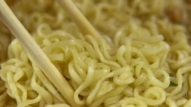 Anında erişteler Çin yemek çubuklarıyla karıştırılır. Yakın plan demlenmiş sarı ramen.