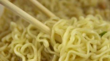 Anında erişteler Çin yemek çubuklarıyla karıştırılır. Yakın plan demlenmiş sarı ramen.