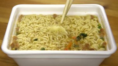 Anında erişteler Çin yemek çubuklarıyla karıştırılır. Özel plastik tabakta demlenmiş sarı ramen.