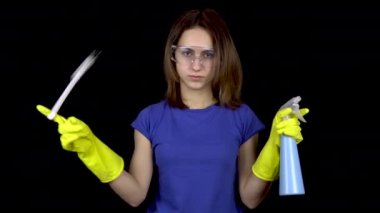 Genç bir kadın parmağındaki tuvalet fırçasını burktu ve sprey şişesinden su serpti. Güvenlik gözlüklü ve eldivenli kadın tuvaleti temizlemek için aletleri var. Kız elinde bir tuvalet fırçası ve sprey tutuyor.