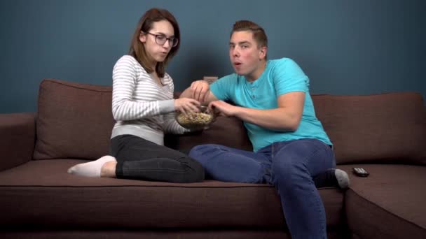 Young man and woman watching TV and eating popcorn. Couple fighting for a plate with popcorn. Watch TV carefully — Stock Video