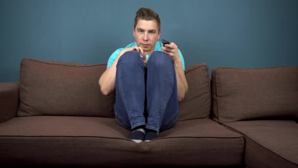 Un joven está viendo televisión y comiendo palomitas de maíz. El tipo está mirando la televisión con cuidado. Un momento emocionante en la trama del programa de televisión. El hombre se subió a los pies en el sofá. La vista desde el televisor. Mirando — Vídeos de Stock