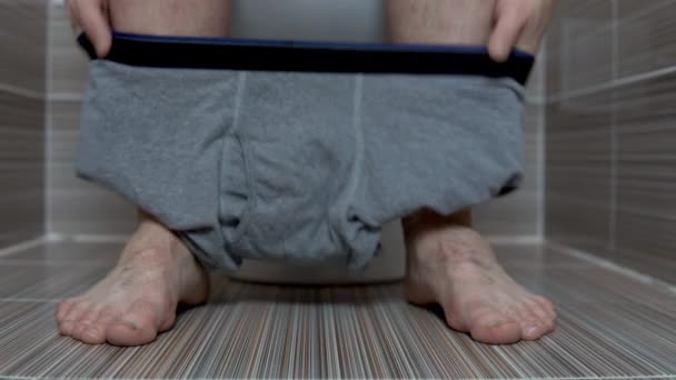 Muž si sundal šedé kalhotky, když seděl na záchodě. Muž s chlupatýma nohama na záchodě — Stock video