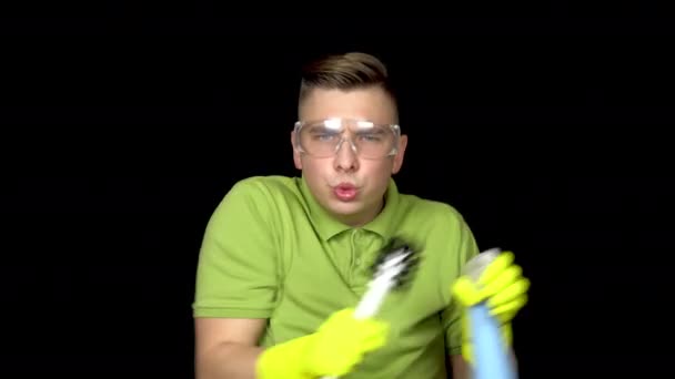 若いトイレ掃除機が踊っている。トイレを掃除するための安全メガネと手袋の男。男はトイレブラシとスプレーを持っています。黒を背景に — ストック動画