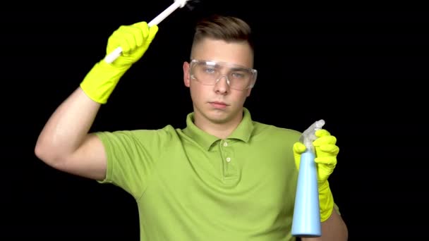 A young man combs his hair with a toilet brush. Man in safety glasses and gloves for cleaning the toilet. The guy holds a toilet brush and spray. On a black background — Stock Video