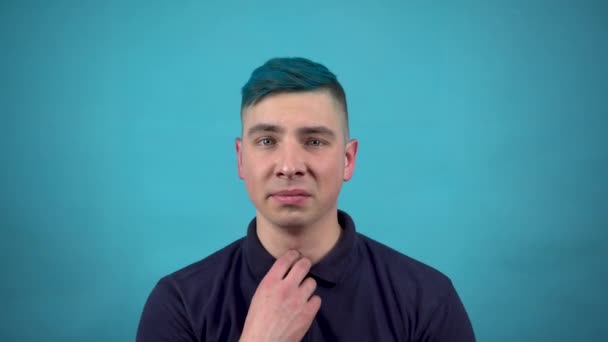 Ein junger Mann mit Brille und blauem Haar ist nervös. Der emotionale Mann ist nervös vor blauem Hintergrund. — Stockvideo