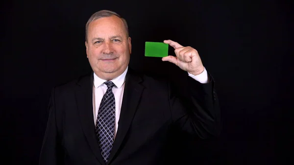 Старий бізнесмен у костюмі тримає банківську картку в руці. Зелена листівка Chromakey. Ізольований чорний фон. 4k — стокове фото