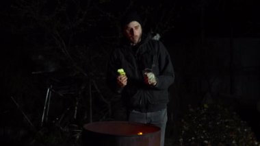 Evsiz genç bir adam ateşin yanında duruyor ve bir elma yiyor. Bir adam gece ateş fıçısının yanında durur ve güneşlenir.