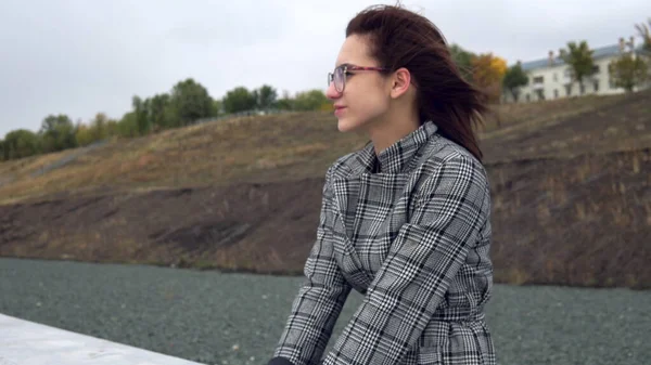 Young woman sits on a concrete fence in the wind — Stock Photo, Image