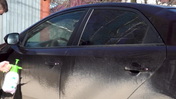 A man puts foam on a car to remove dirt. Special detergent for car wash. Washes a car in front of the house.