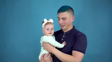 Mavi saçlı genç bir baba kucağında bir bebek tutuyor. Çocuklu alternatif adam mavi arka plandaki kameraya bak..