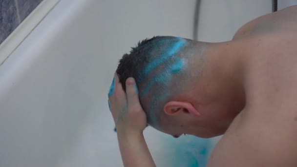 Młody mężczyzna z niebieskimi włosami myje głowę. Mężczyzna zmywa niebieską farbę z włosów. — Wideo stockowe