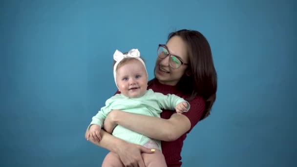 Een jonge moeder houdt een baby in haar armen. vrouw met een dochter op een blauwe achtergrond. — Stockvideo