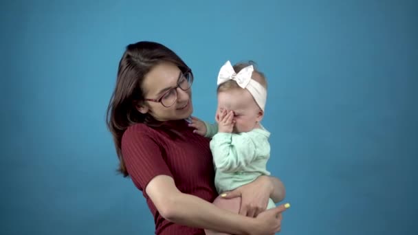 Een jonge moeder houdt een baby in haar armen. vrouw met een dochter op een blauwe achtergrond. — Stockvideo