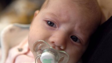 Annesinin kollarında bir bebek. Bir çocuk kuklayı emer ve kameraya bakar. Yüzünü kapat.