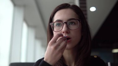 Kızarmış patates yiyen genç bir kadın. Bir kız panoramik pencerenin yanındaki kafede oturur ve fast food yer..