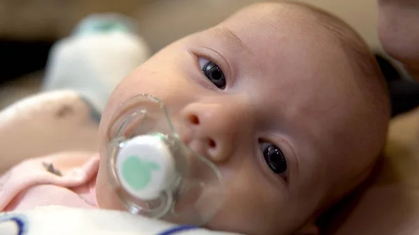 Baby in the arms of her mother. A child sucks a dummy and looks at the camera. Face close up — Stock Photo, Image