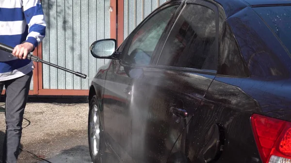 Un hombre lava la tierra de un coche con un chorro de agua de alta presión. Detergente especial para lavado de autos. Lava un coche delante de la casa . — Foto de Stock